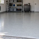 Szürke, finoman érdesített műgyanta garázspadló autóval és rendezett tárolópolcokkal.
