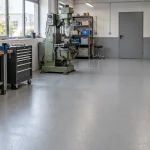 Szürke műgyanta padló rendezett műhelyben, munkapaddal és szerszámkocsival.